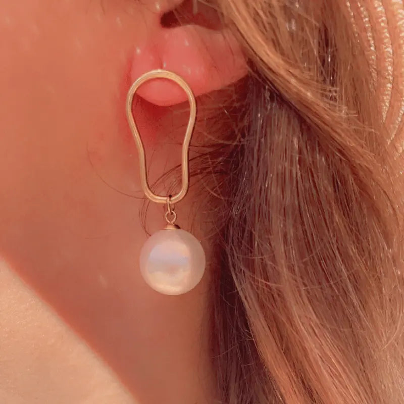 Boucle d'oreille en acier inoxydable avec perle pendante, portée pour un look raffiné.