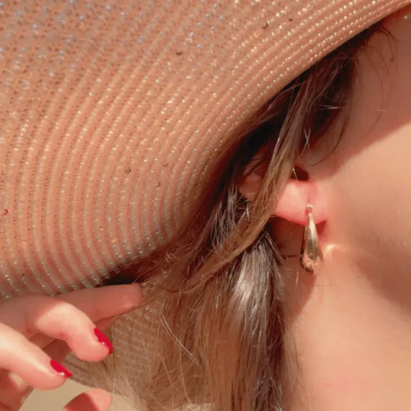 Boucle d'oreille en acier inoxydable dorée en forme de goutte, portée avec un chapeau