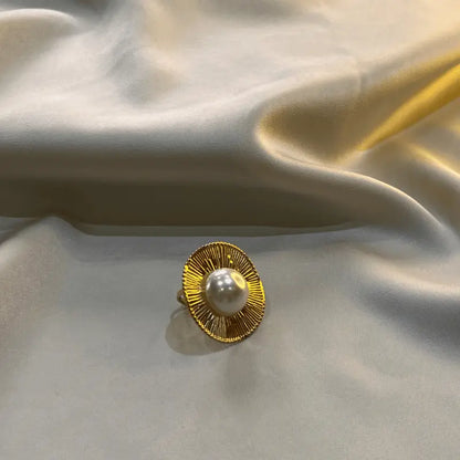 Bague en acier inoxydable dorée avec une perle, posée sur un fond en tissu brillant
