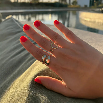 Bague Iris et Giulia en acier inoxydable dorée avec un design unique, portées sur une main près de la piscine