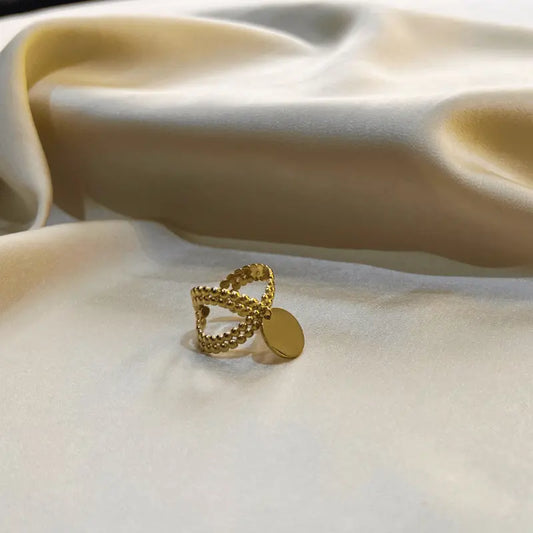 Bague breloque en acier inoxydable dorée avec design d'anneaux, posée sur un fond en tissu
