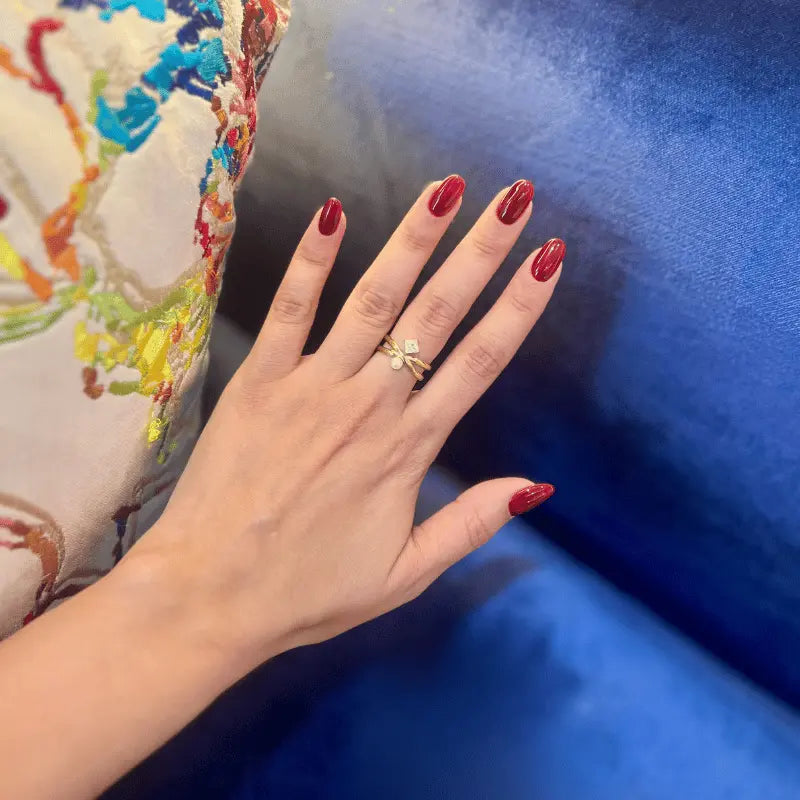 Bague en acier inoxydable dorée avec perle et pierre, portée sur une main avec un fond coloré