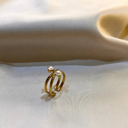 Bague en acier inoxydable dorée avec double anneau, ornée d'une perle et d'une pierre, posée sur un fond en tissu