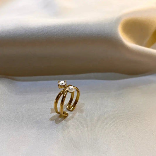 Bague en acier inoxydable dorée avec double anneau, ornée d'une perle et d'une pierre, posée sur un fond en tissu