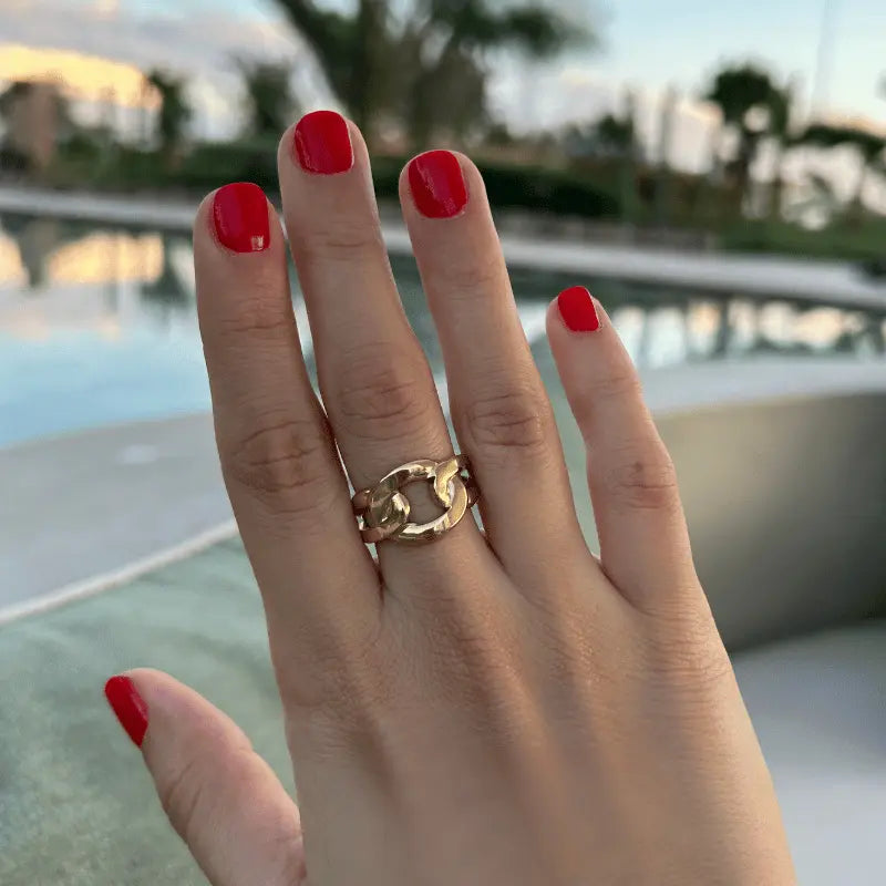 Bague en acier inoxydable dorée avec un design de maillons, portée sur une main avec un fond de piscine