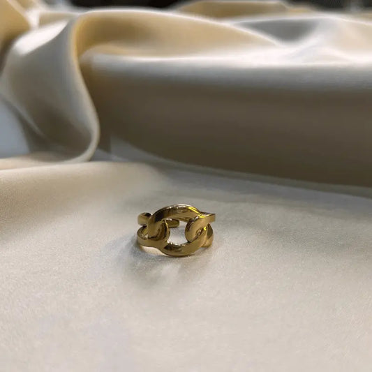 Bague en acier inoxydable dorée avec un design de maillons, posée sur un fond en tissu