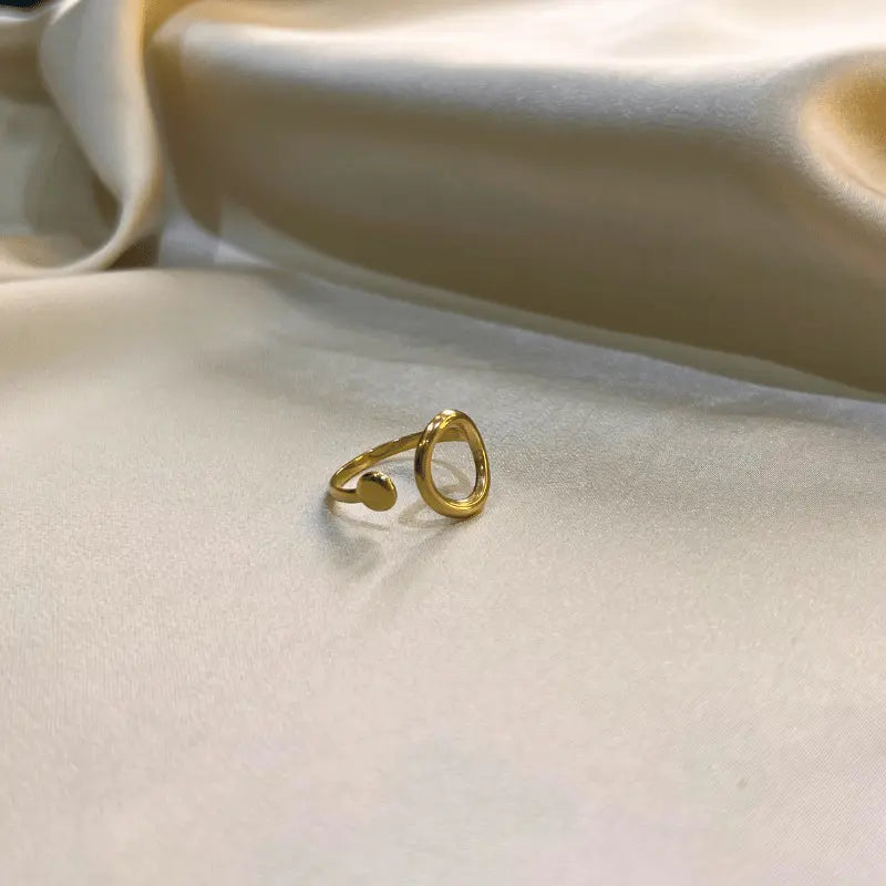 Bague minimaliste en acier inoxydable dorée avec un design ouvert, posée sur un fond en tissu