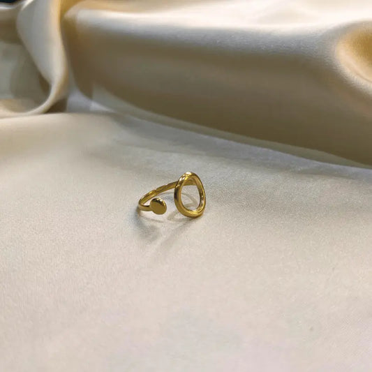 Bague minimaliste en acier inoxydable dorée avec un design ouvert, posée sur un fond en tissu