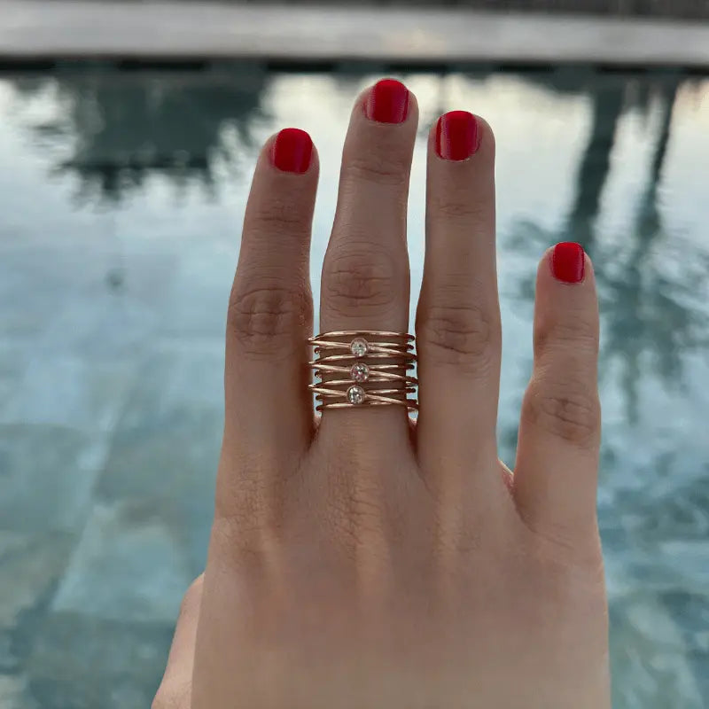 Main ornée d'une bague multi-rangs en acier inoxydable doré, avec un arrière-plan de piscine