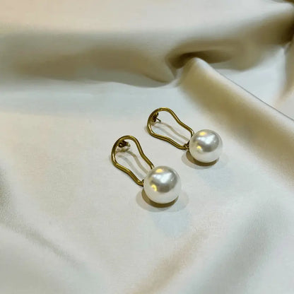 Boucles d'oreilles en acier inoxydable avec perles élégantes, posées sur un fond satiné.