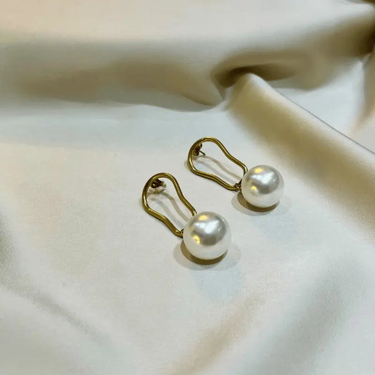 Boucles d'oreilles en acier inoxydable avec perles élégantes, posées sur un fond satiné.
