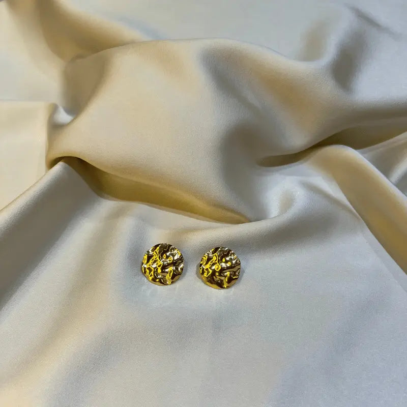 Boucles d'oreilles rondes en acier inoxydable avec une texture martelée, posées sur un fond en tissu