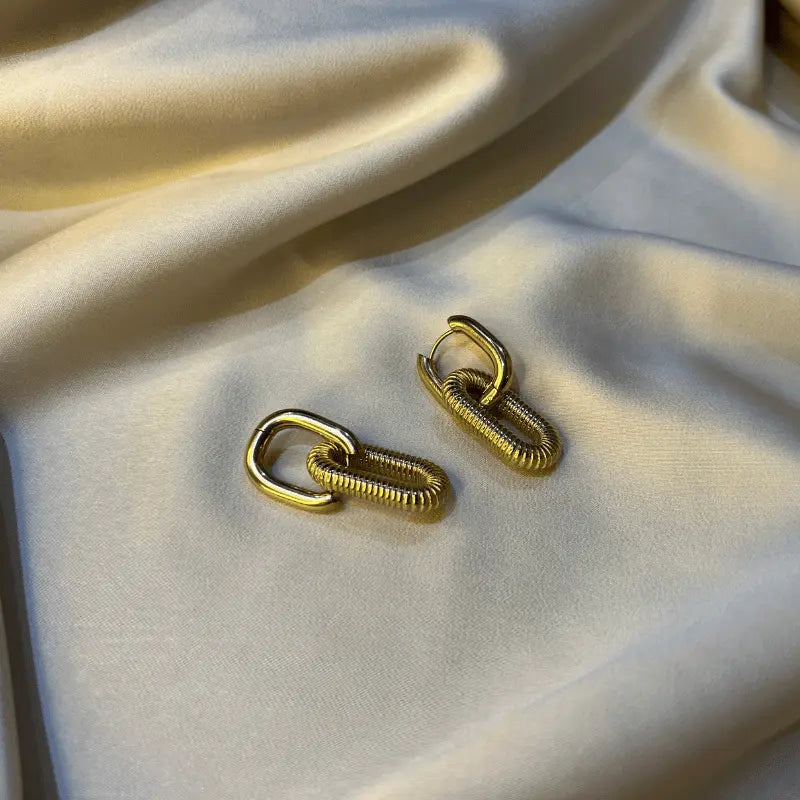 Gros plan sur une paire de boucles d’oreilles dorées en acier inoxydable, affichant un design de chaînes élégantes.