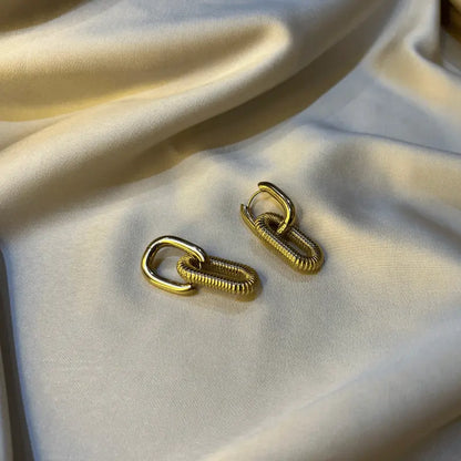 Gros plan sur une paire de boucles d’oreilles dorées en acier inoxydable, affichant un design de chaînes élégantes.