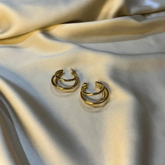 Boucles d'oreilles créoles en acier inoxydable dorées, posées sur un fond en tissu