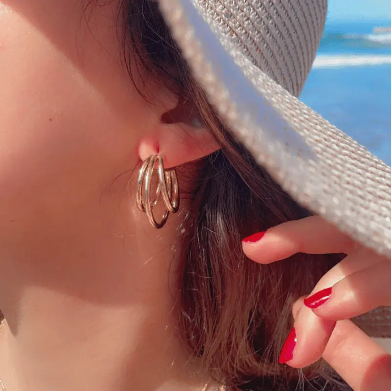 Boucles d'oreilles créoles zina en acier inoxydable dorées, portées avec un chapeau en extérieur