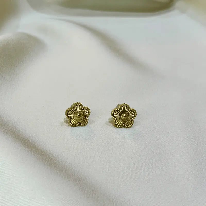 Boucles d'oreilles en acier inoxydable dorées en forme de fleur, posées sur un fond en tissu sous un autre angle