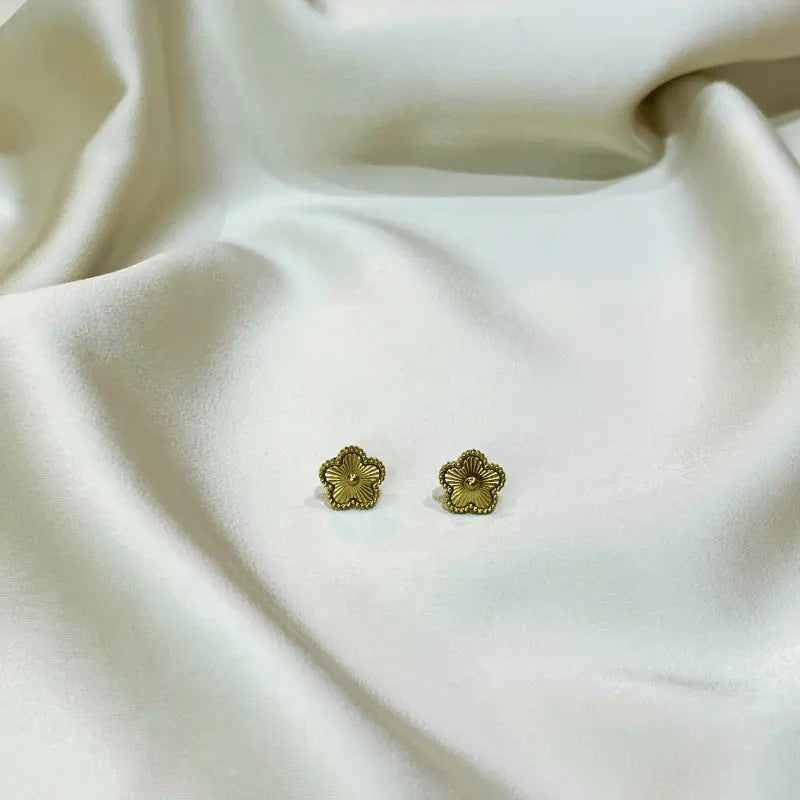 Boucles d'oreilles en acier inoxydable dorées en forme de fleur, posées sur un fond en tissu