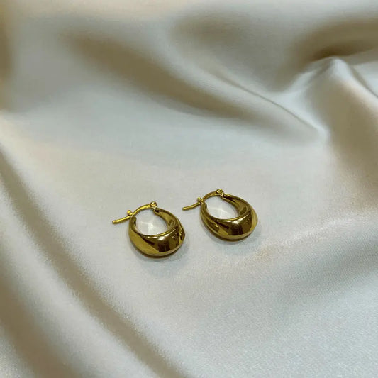 Boucles d'oreilles en acier inoxydable dorées en forme de goutte, posées sur un fond en tissu sous un angle différent