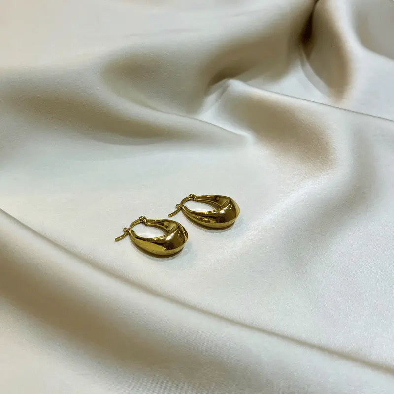 Boucles d'oreilles en acier inoxydable dorées en forme de goutte, posées sur un fond en tissu
