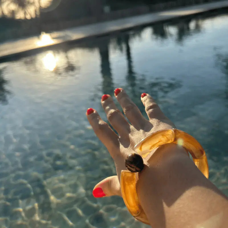 Bracelet en acétate couleur marron, porté en extérieur au bord de la piscine.