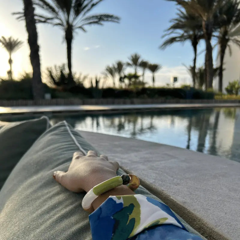 Bracelet en acétate multicolore, porté en extérieur près d'une piscine.