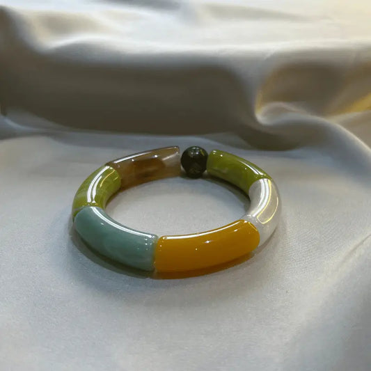 Bracelet en acétate multicolore vert, posé sur un fond de tissu soyeux.