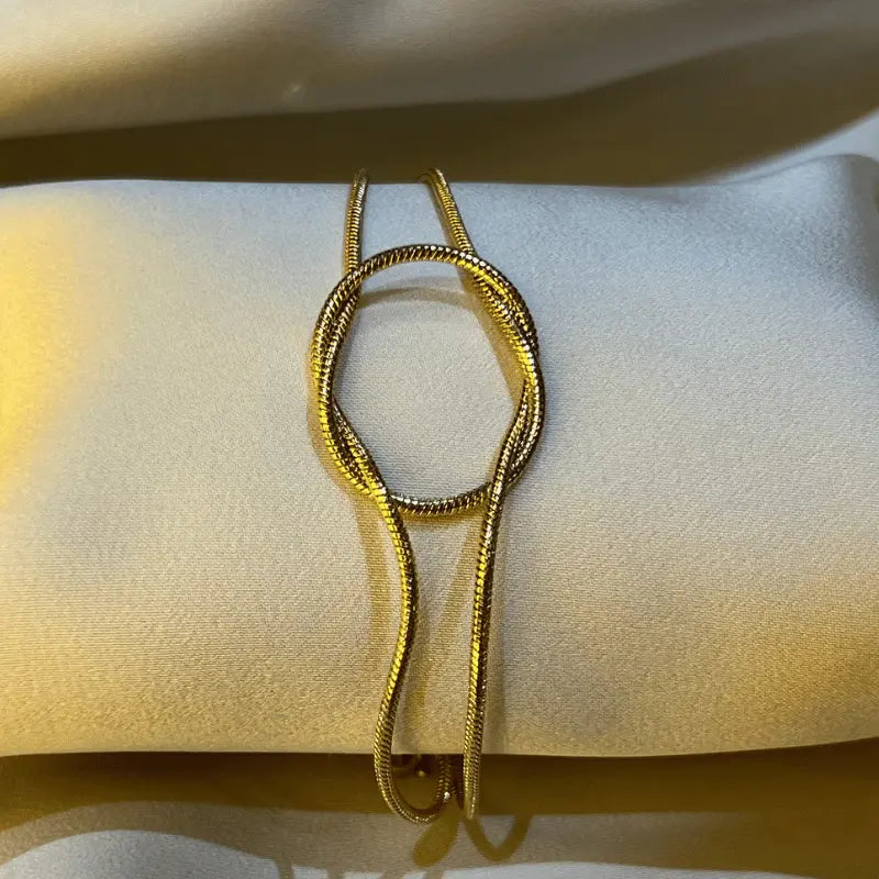 Gros plan sur un bracelet doré en acier inoxydable, posé sur un fond en tissu.