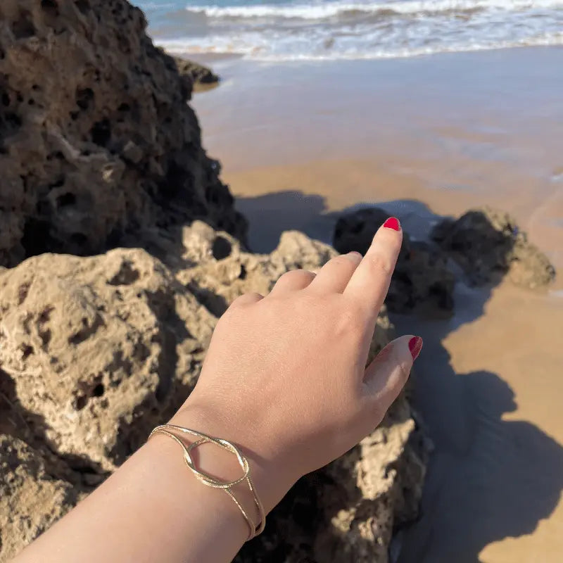 Bracelet en acier inoxydable doré, porté en extérieur avec vue sur la plage.