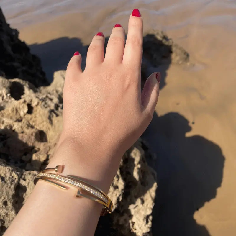 Bracelet doré avec strass porté en bord de mer, mettant en avant un design élégant en acier inoxydable.