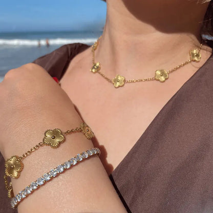 Bracelet et collier en acier inoxydable dorés avec motifs floraux, portés en extérieur avec vue sur la mer