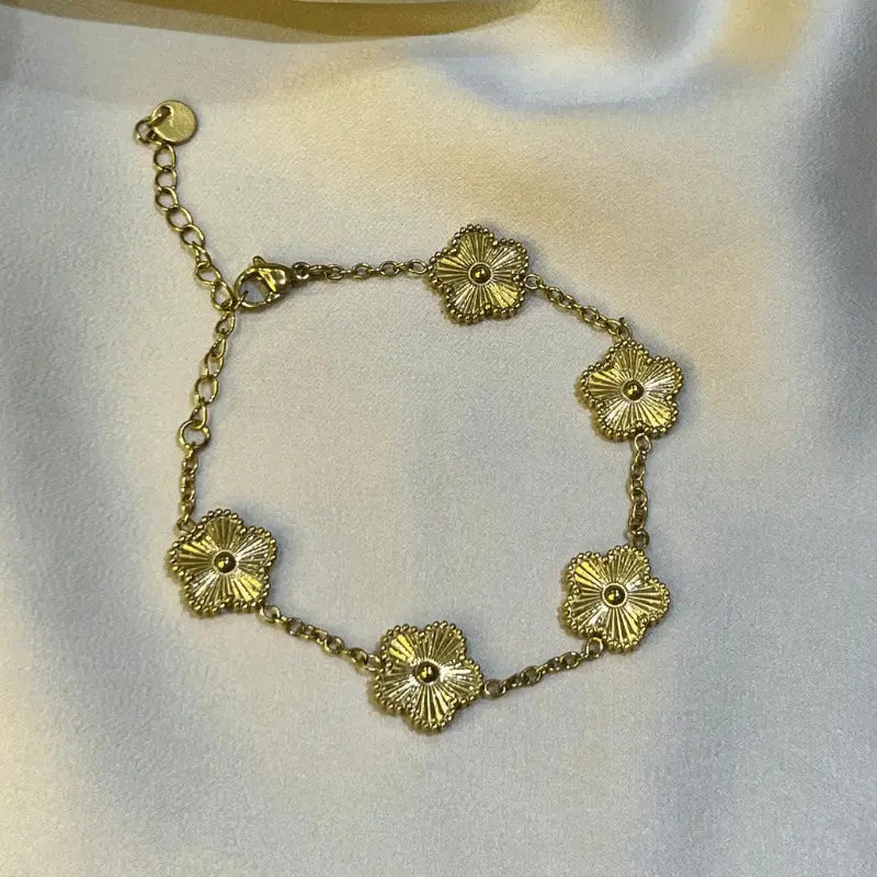 Bracelet en acier inoxydable doré avec motifs floraux en gros plan, posé sur un fond en tissu