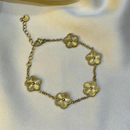 Bracelet en acier inoxydable doré avec motifs floraux en gros plan, posé sur un fond en tissu