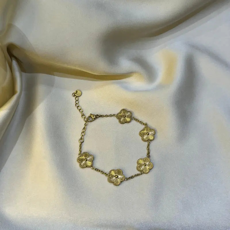 Bracelet en acier inoxydable doré avec motifs floraux, posé sur un fond en tissu