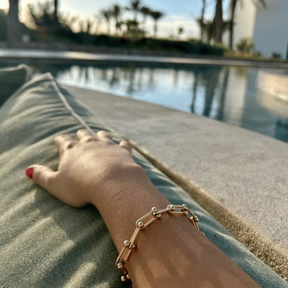 Bracelet en acier inoxydable doré à maillons, porté près d'une piscine pour un look élégant en extérieur