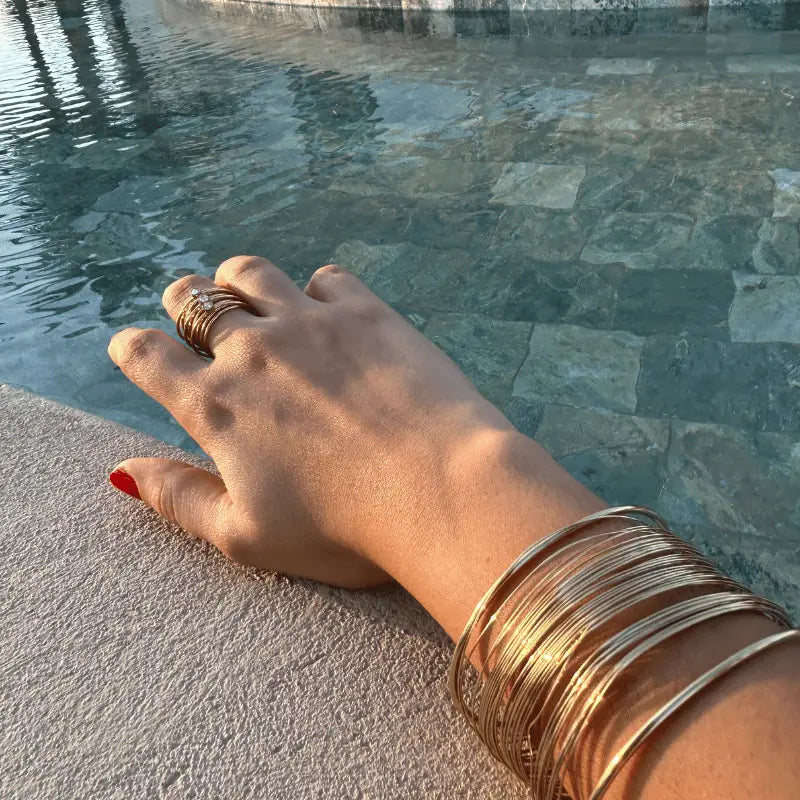 Bracelet manchette et bague multirangs en acier inoxydable doré portée près de la piscine
