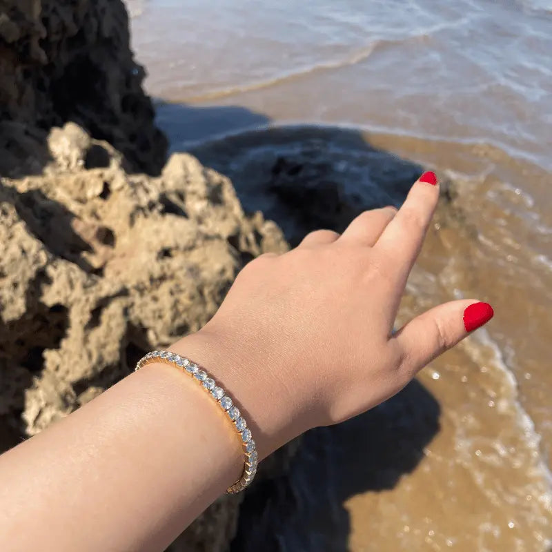 Bracelet en acier inoxydable doré orné de pierres brillantes, porté en extérieur avec vue sur la mer