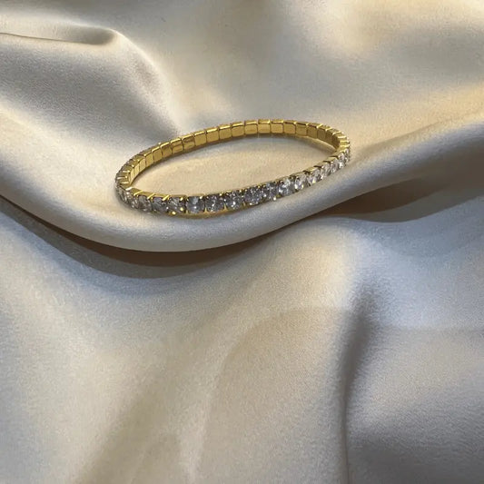Bracelet en acier inoxydable doré avec une rangée de pierres brillantes, posé sur un fond en tissu
