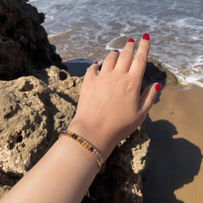 Bracelet en acier inoxydable doré avec pierres colorées, porté en extérieur sur fond de plage, variant de couleurs éclatantes