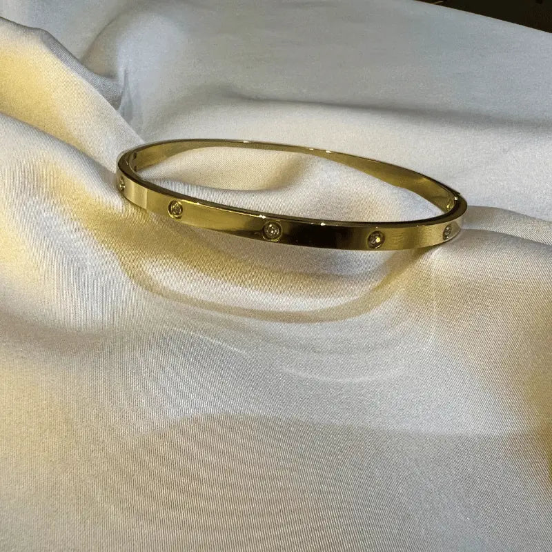 Bracelet rigide en acier inoxydable doré avec incrustations de pierres, en gros plan sur fond en tissu