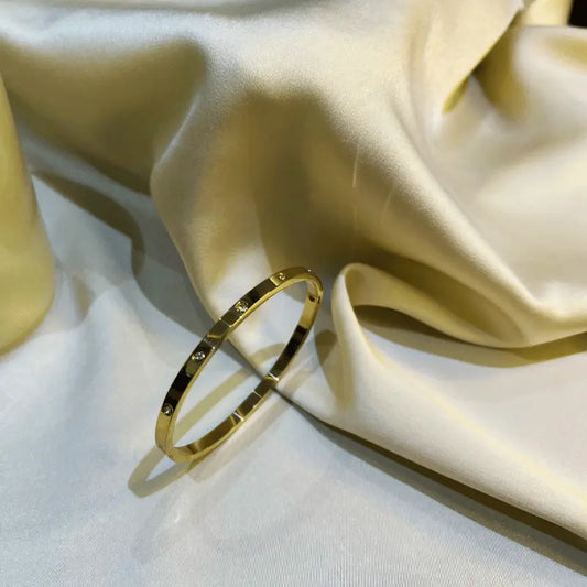 Bracelet rigide en acier inoxydable doré avec incrustations de pierres, posé sur un fond en tissu
