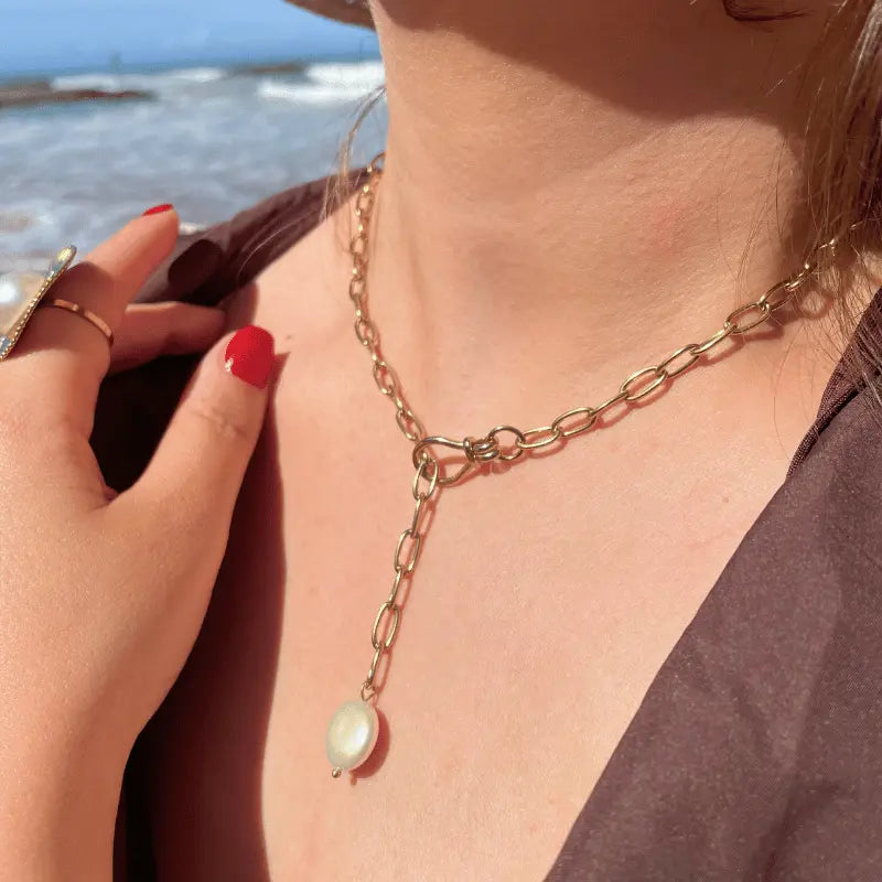 Collier  en acier inoxydable avec une chaîne dorée et une perle et bague perle, porté en extérieur près de la mer