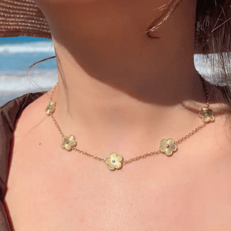 Collier en acier inoxydable doré avec motifs floraux, porté en extérieur avec vue sur la plage