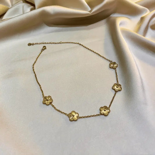 Collier en acier inoxydable doré avec motifs floraux, posé délicatement sur un fond en tissu