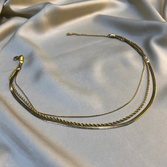 Collier multi-rangs en acier inoxydable doré, posé élégamment sur un fond en tissu.