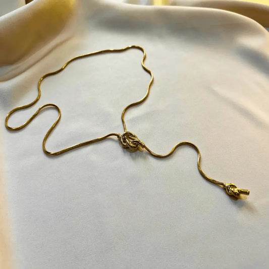 Collier en acier inoxydable avec un nœud décoratif, posé délicatement sur un tissu doux